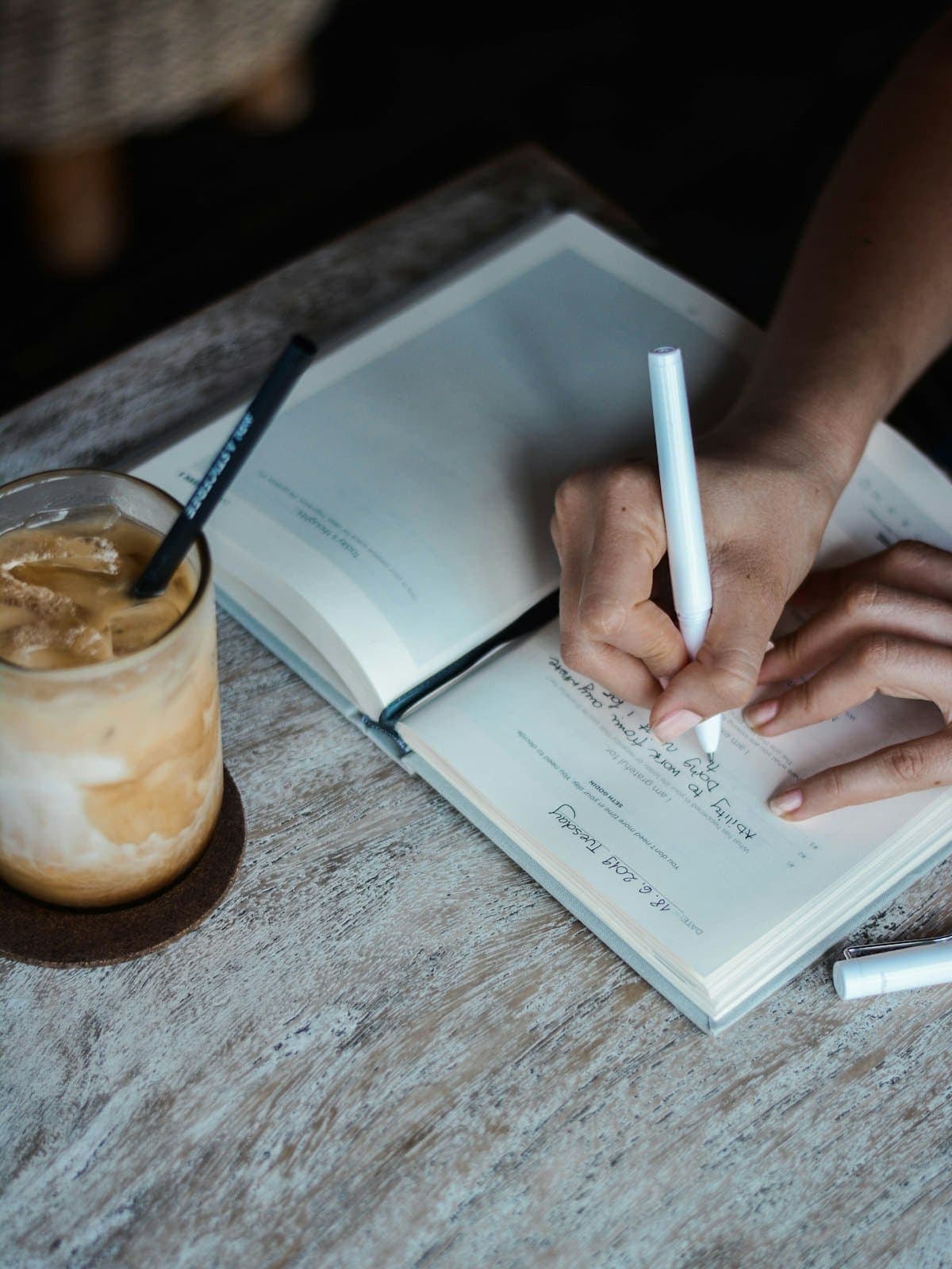 Someone writing in a journal beside a coffee